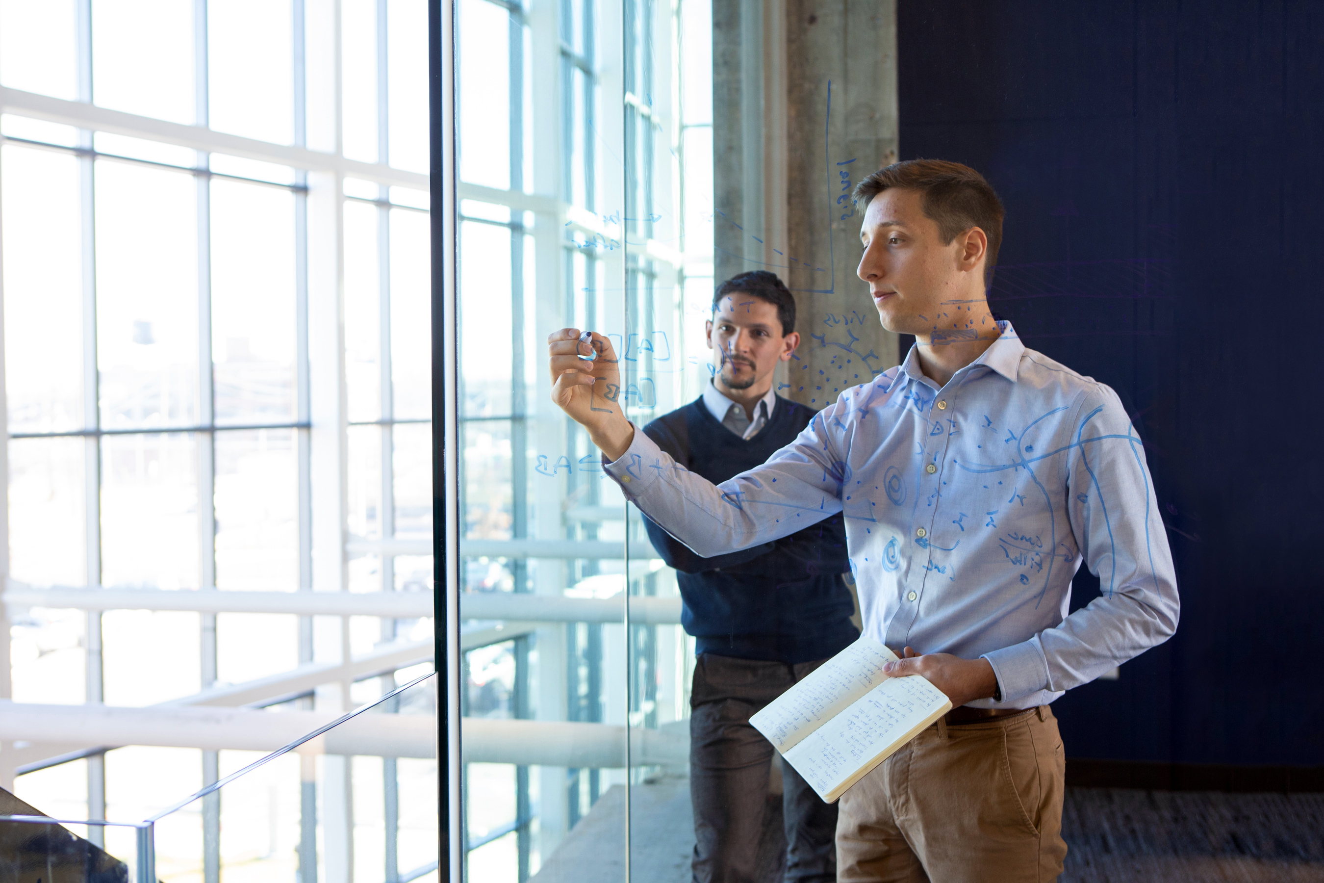Two University of Cincinnati students write on a transparent board