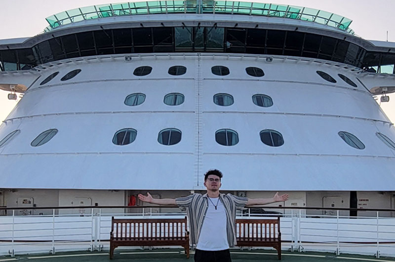 A person standing on the deck of a cruise ship during sunset.
