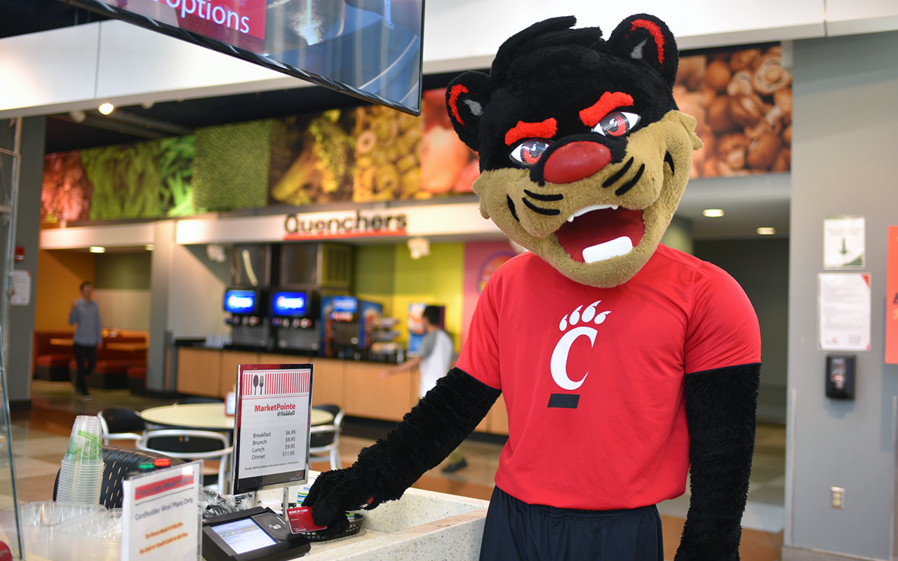 Mascot swiping Bearcat Card at dining center cashier stand