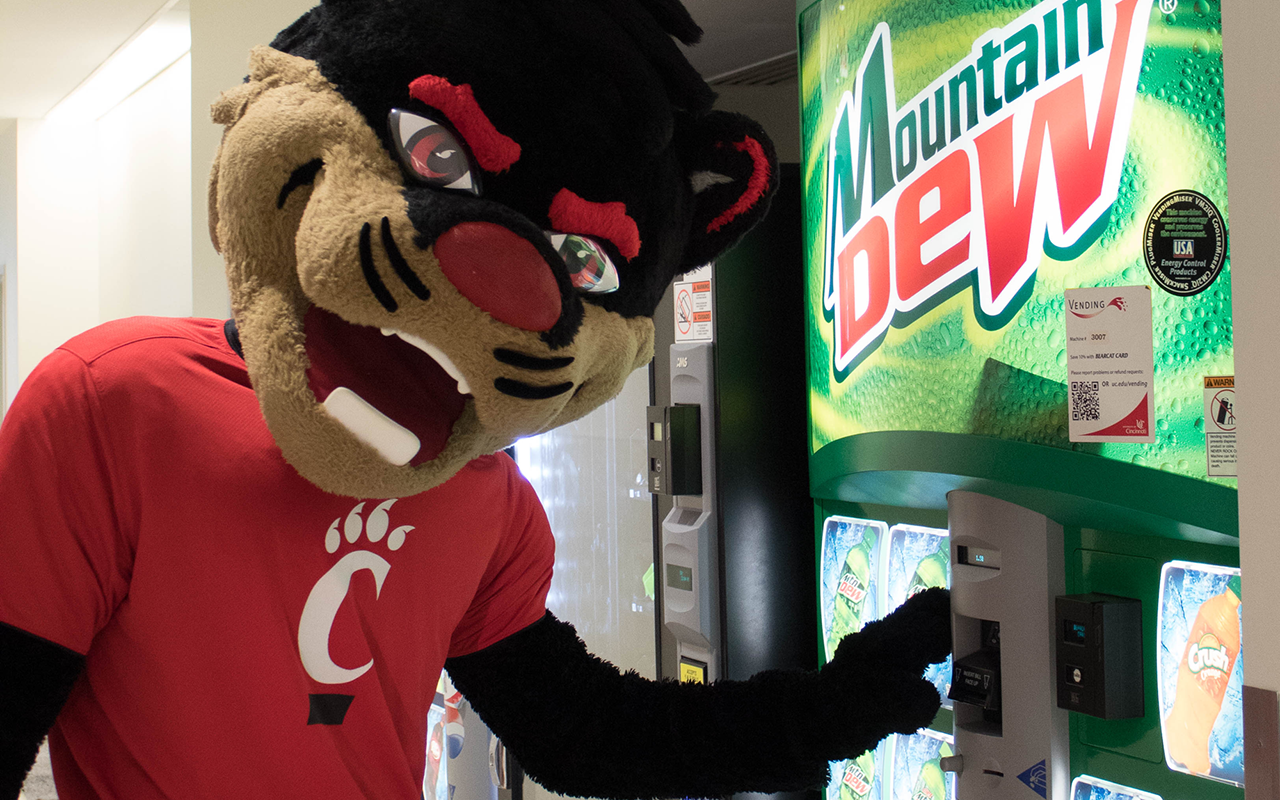 Bearcat mascot standing next to beverage vending machine