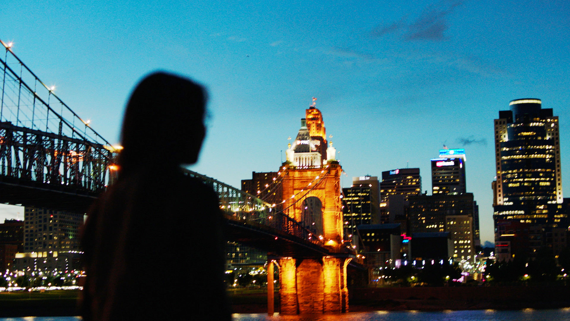 A student is silhouetted in the foreground of a view of the Cincinnati skyline at dusk
