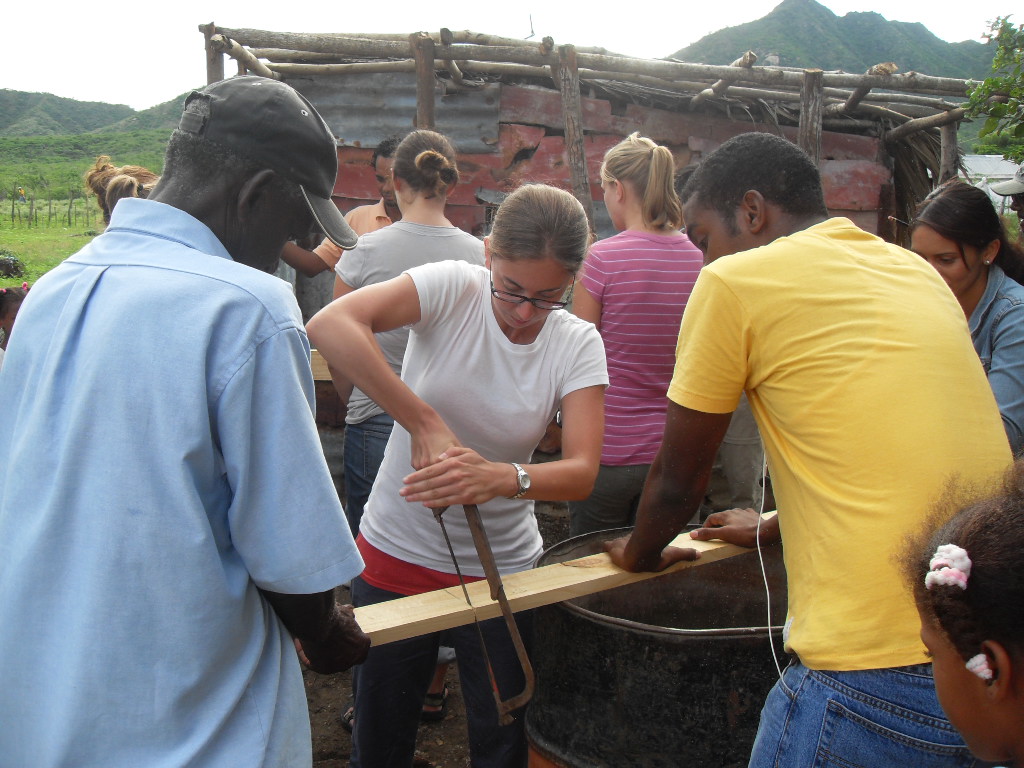 Randi Bates uses a saw on a piece of wood while working with seven other people to build a chicken coop as part of her Peace Corps work