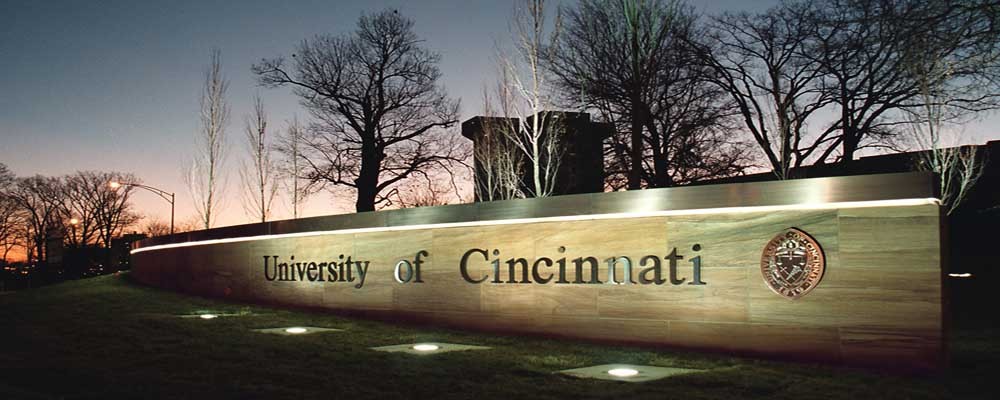 The University of Cincinnati sign is lit up at dusk by lights.
