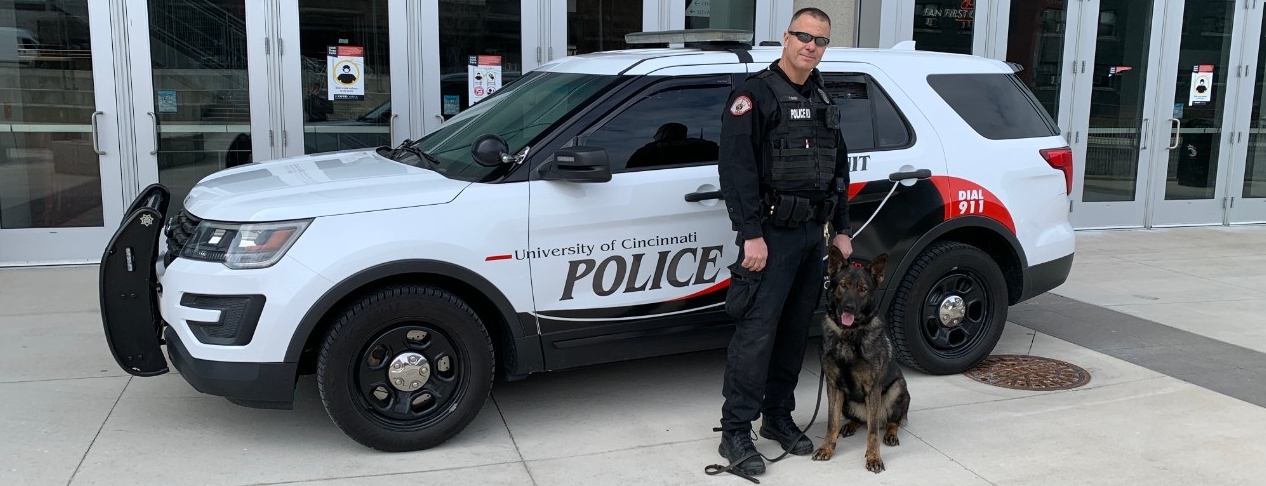 Officer Lance Long poses with K-9 Bert in front of a cruiser.
