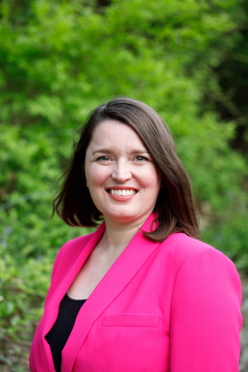 Amy smiling outdoors in a pink jacket.