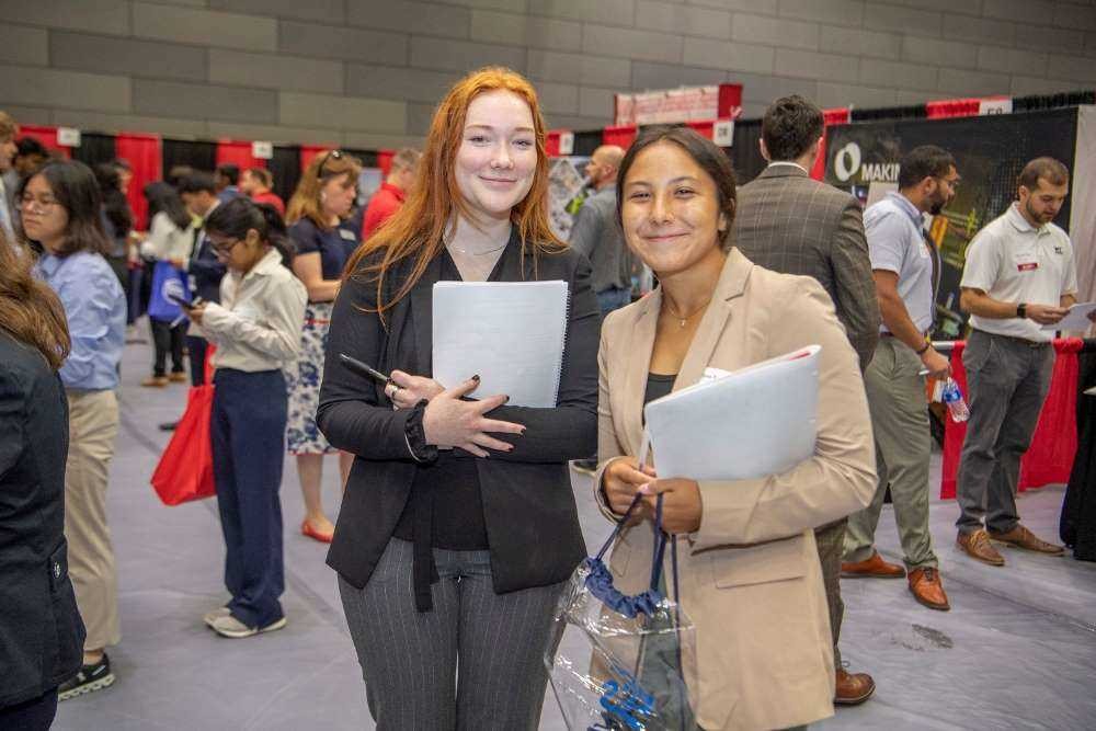 two young women in business jackets pose for the camera