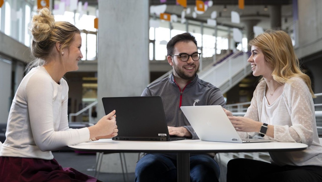 three young people around a table with laptops in a modern office