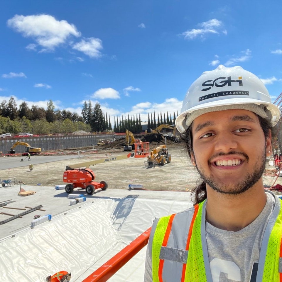a student wears a hard hat while taking a selfie on a co-op site. 