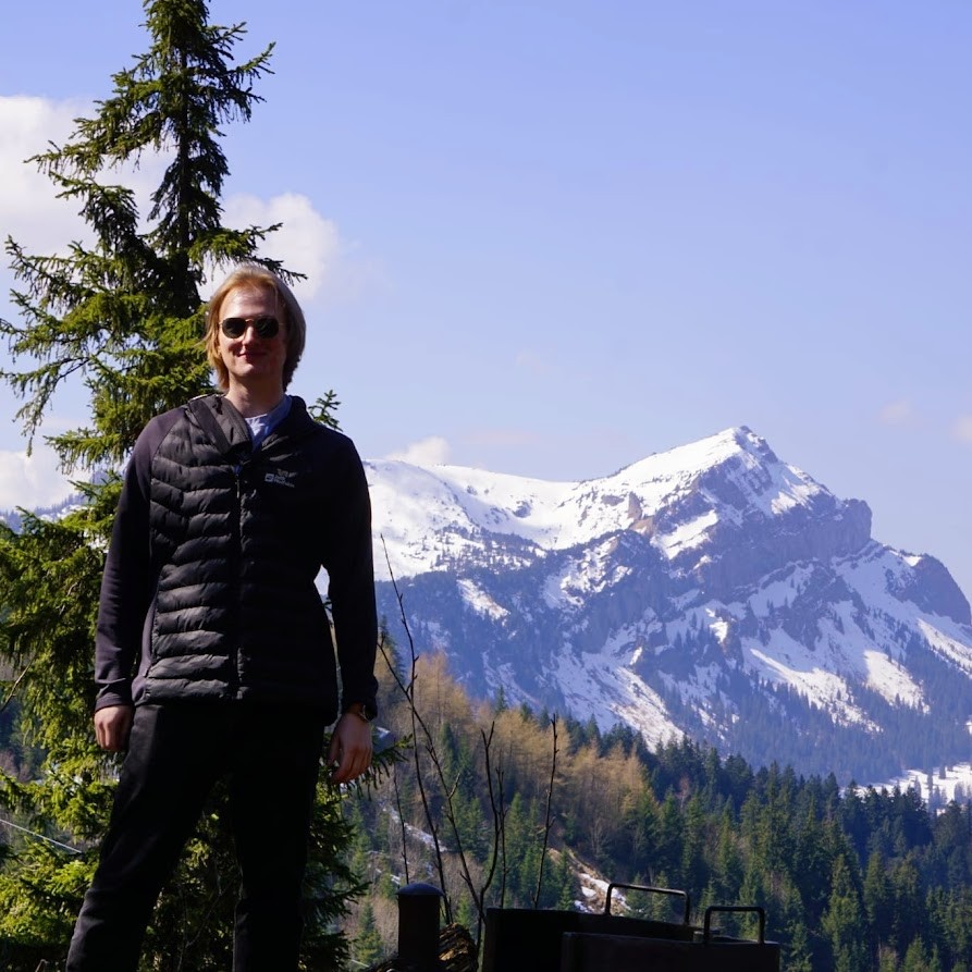 Person standing in front of a snow-capped mountain on a sunny day