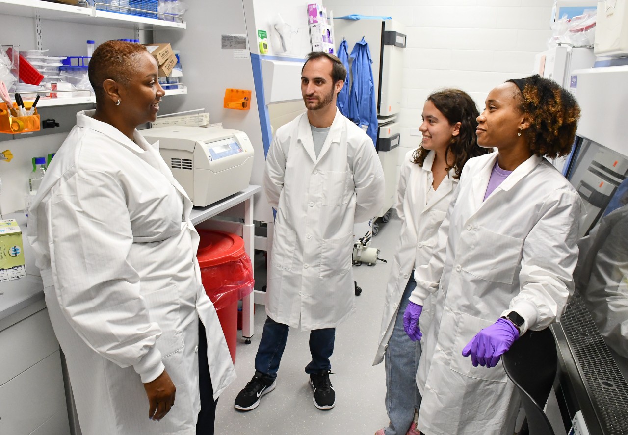Four scientists in lab coats are engaged in a discussion in a laboratory.
