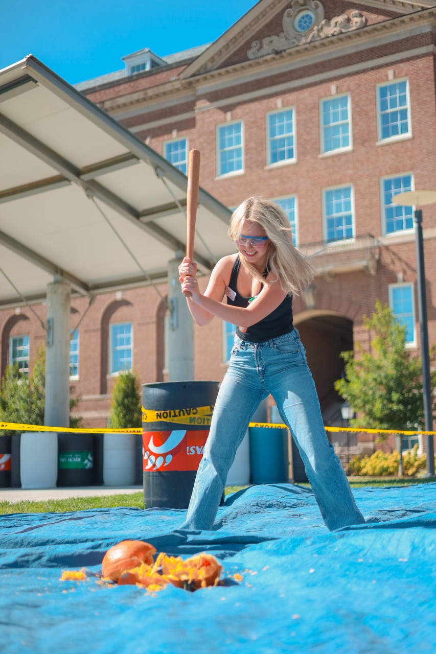 Student at a PAC event in fall 2023, "Pumpkin Palooza", smashing a pumpkin