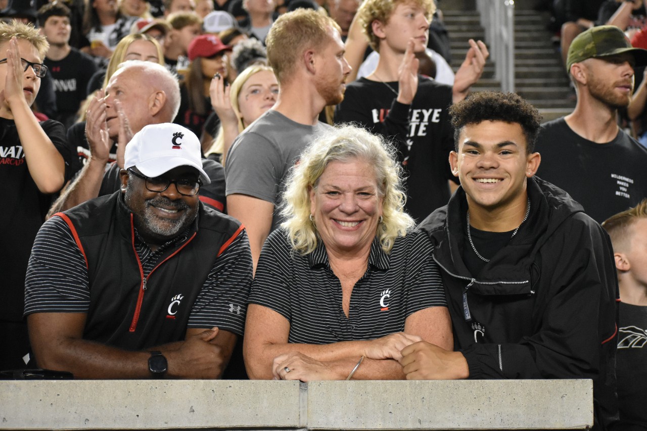 Photo 1: A mom and student show their drawings of the Bearcat. Photo 2: A family poses with the UC Bearcat, who is dressed in workout clothing.  Photo 3: Family members pose with their student in front of a UC Family Weekend Sign. 