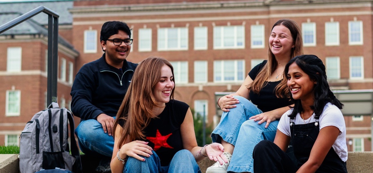 Four students sitting on the steps in front of Arts and Sciences talking 