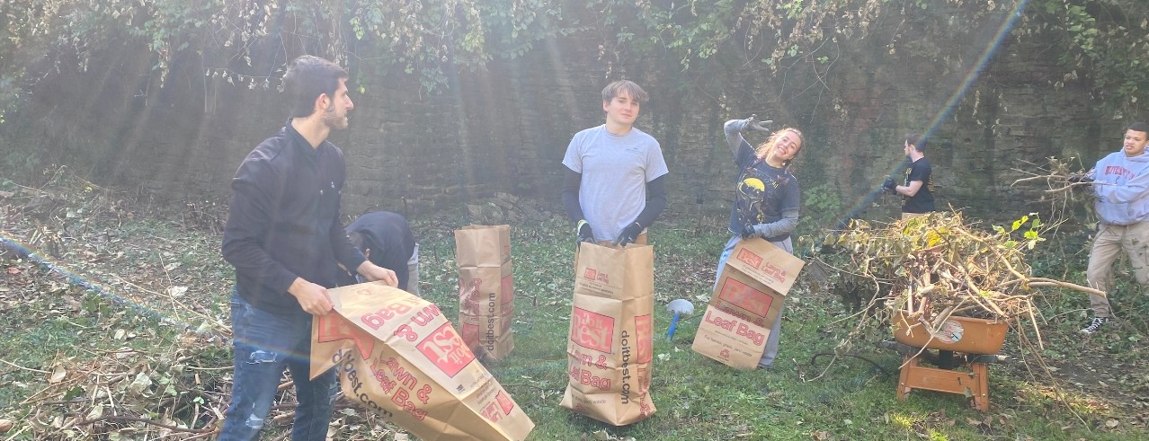 Students standing outside with yard waste bags on a sunny fall day