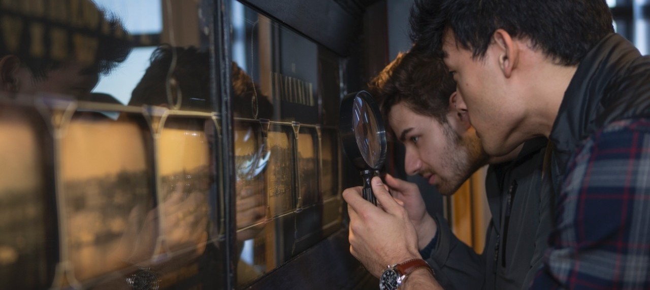 Students in honors seminar look at an exhibit through a magnifying glass