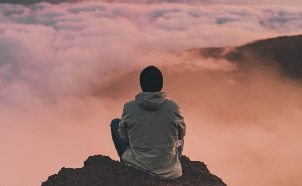 Person sitting on a cliff over a sea of clouds