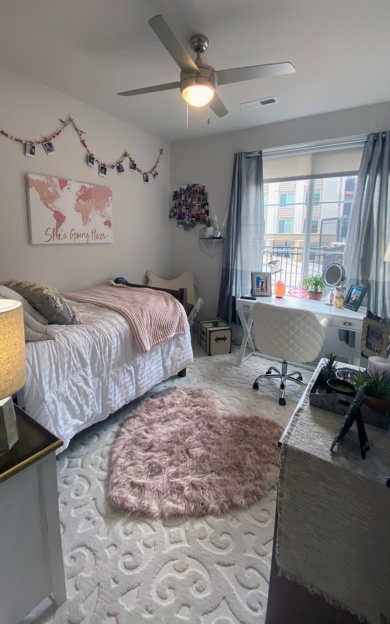Residence hall bedroom featuring heart throw rug on floor with gray and rose accented art and accessories