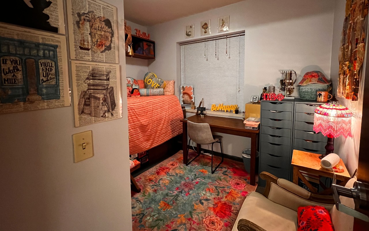 Bed with orange linens and a shelf above the bed, a blue and orange rug on the floor
