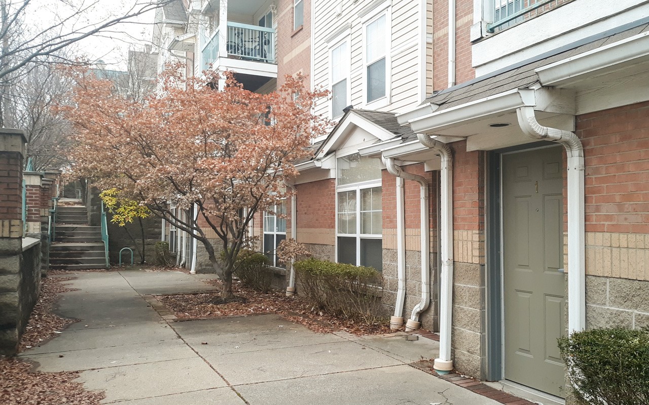 Walkway in front of an apartment door at Bellevue Gardens. There is a small tree on the right past the door.