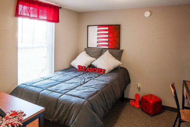 A full-sized bed sits next to a large window, with the bedroom door, dresser and desk in view.