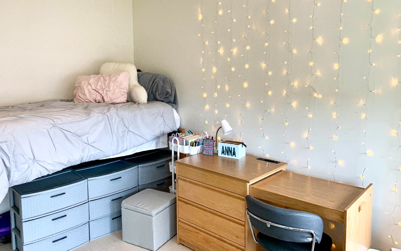 Twin bed rests along wall with decorations at the head of the bed. A desk and drawers sit next to the head of the bed.