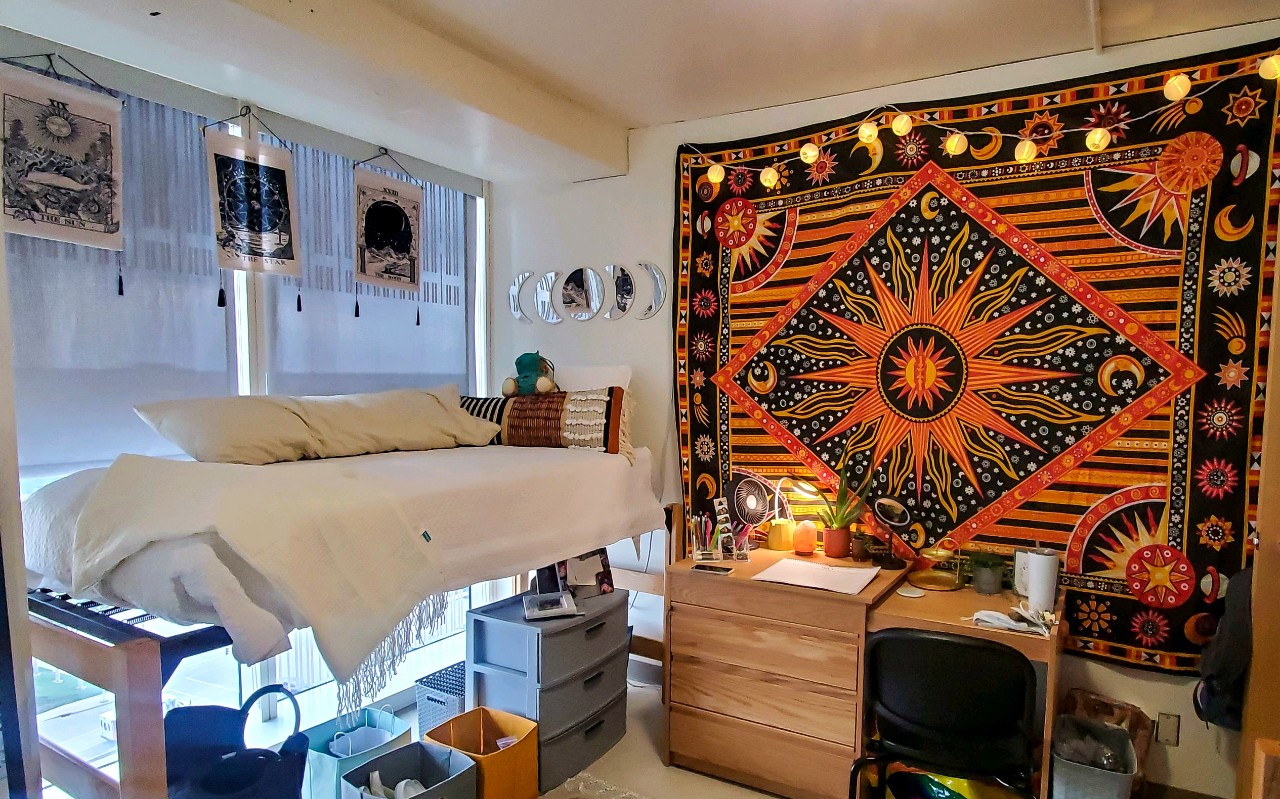 Twin bed rests along wall with decorations at the head of the bed. A desk and drawers sit next to the head of the bed.