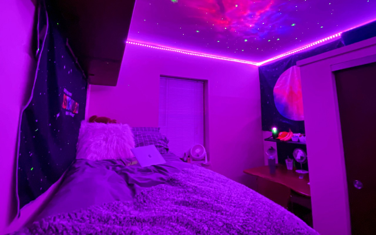LED's light up a room with a twin bed and tapestry's along the walls. 
