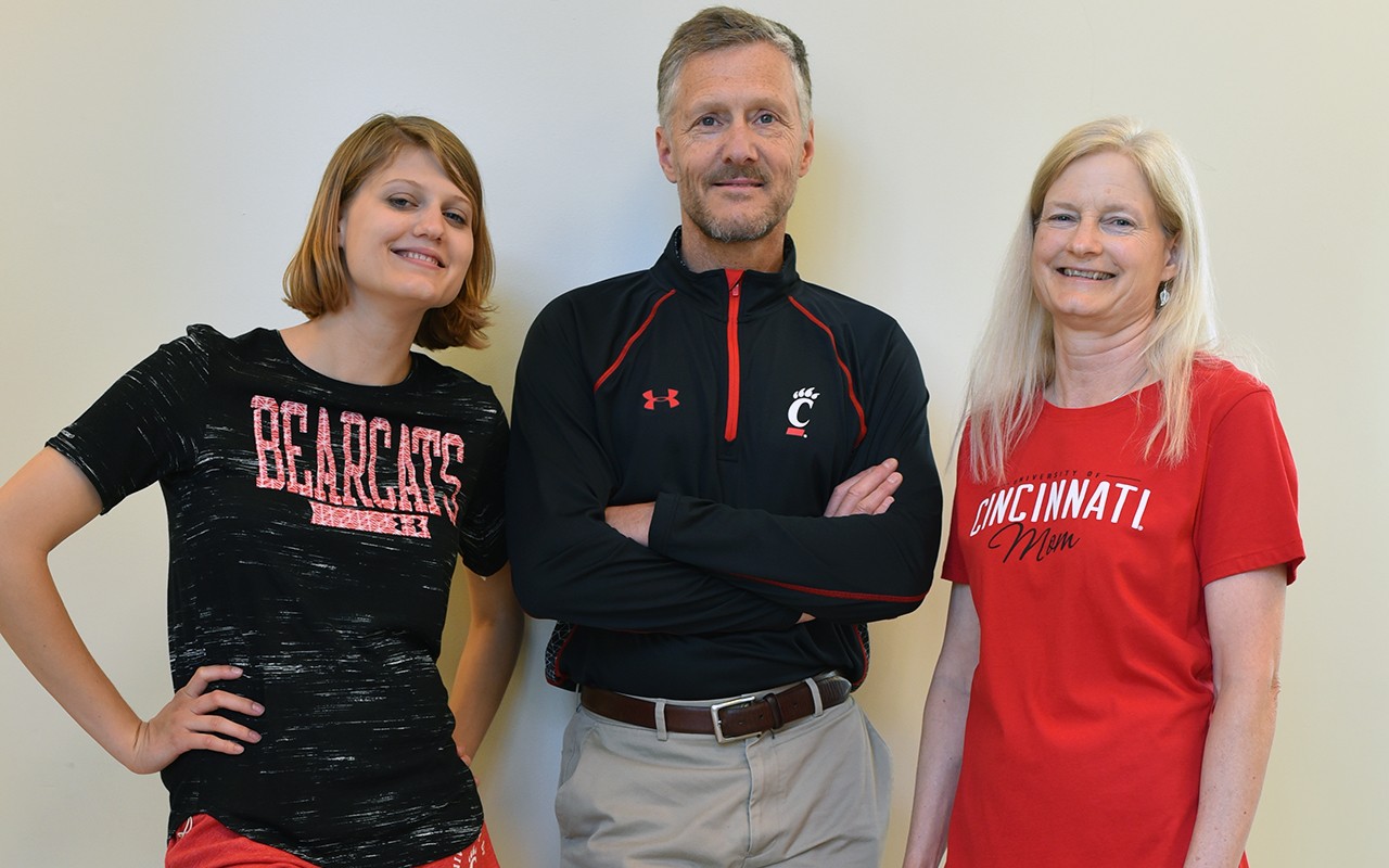 A student with her parents are each wearing UC printed shirts.