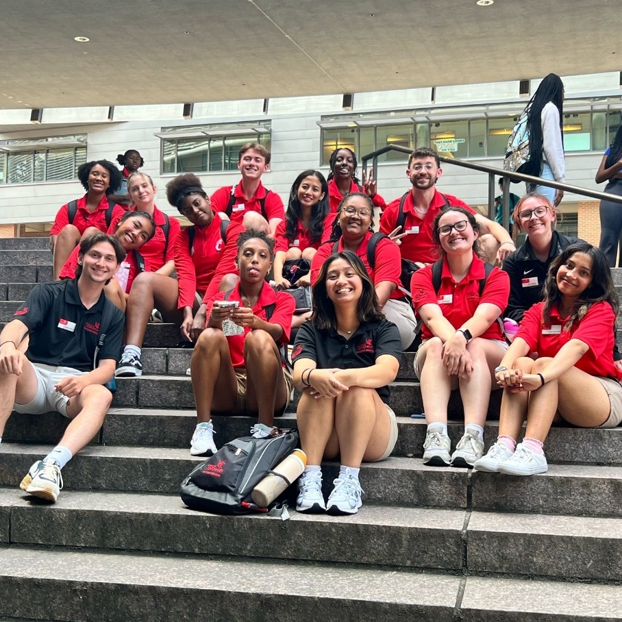 a group of student orientation leaders sit on the large steps outside Mainstreet on UC's campus. 