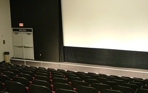 Cinema featuring large screen at front of room with cushioned seating.