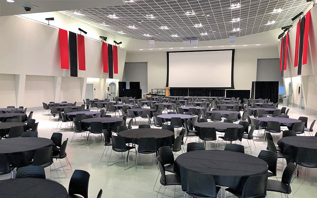 Round tables set up banquet style with large screen at front of room; banners hang from high walls.