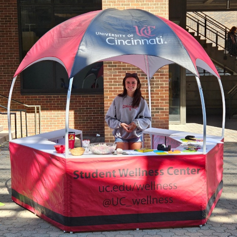 Student standing in pop up tent with striped red and black roof and hexagonal shape. 
