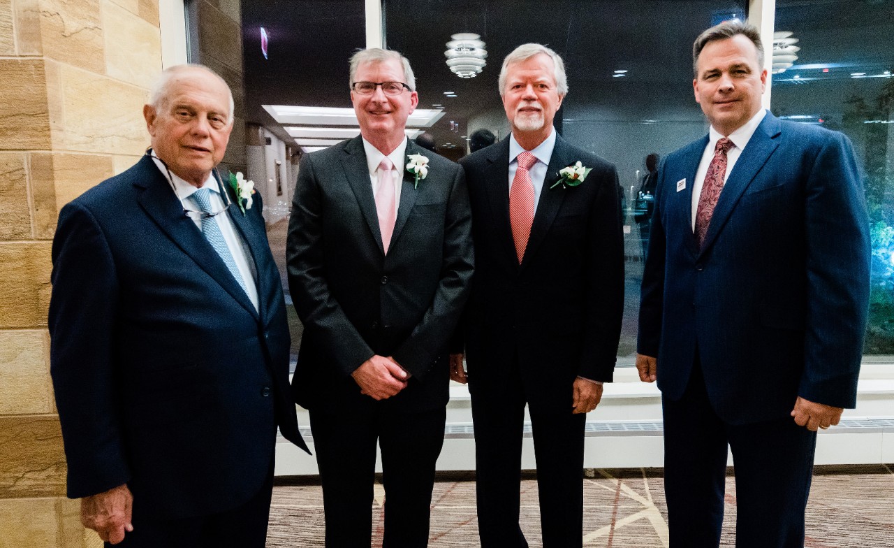 Schueler with three other men in suits at ceremony.