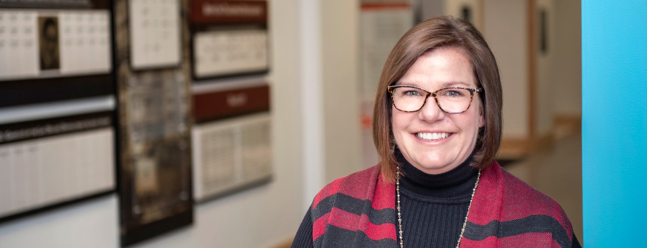 Kelly Epplen standing by a wall of awards in the College of Pharmacy