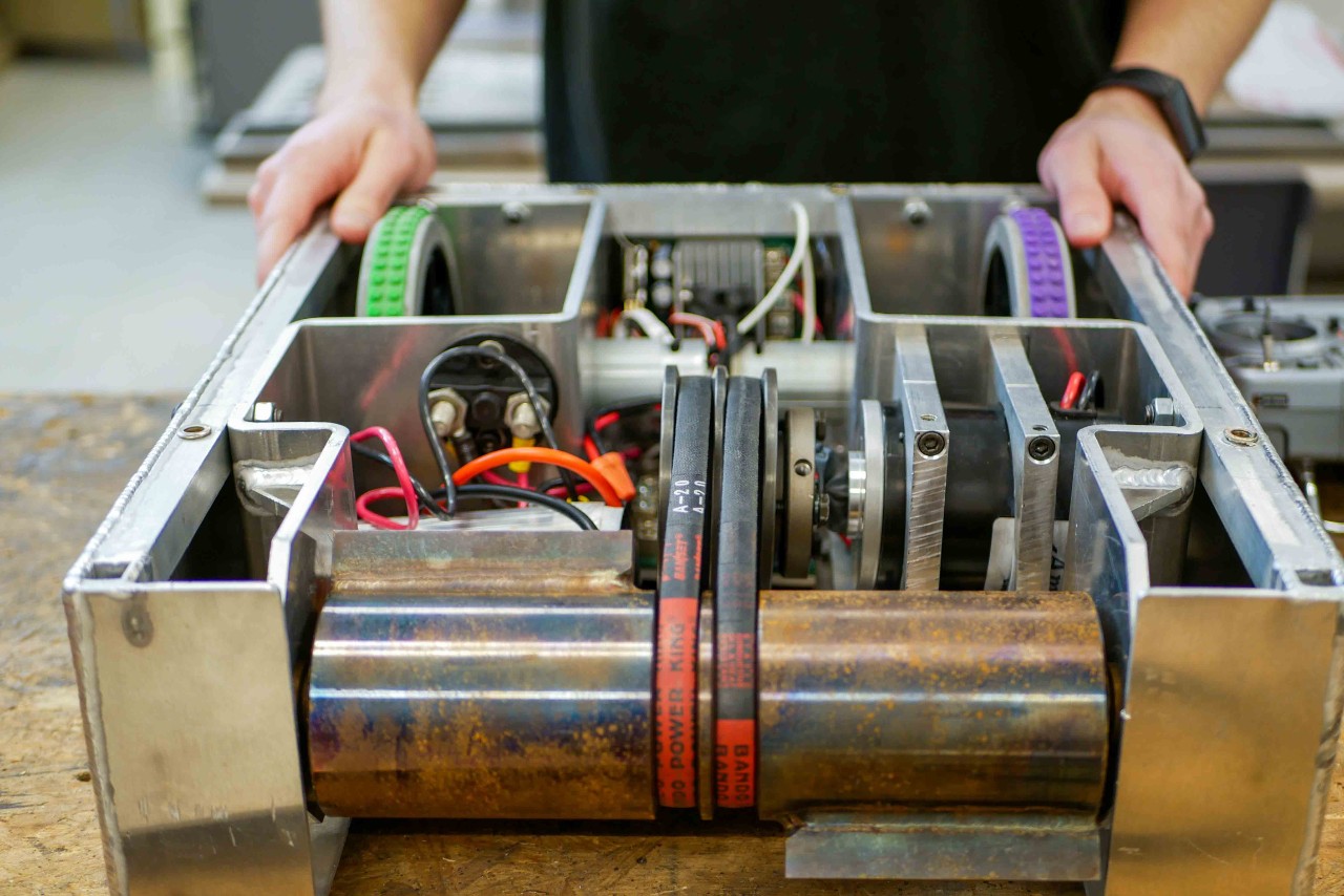 A closeup of  someone holding the innards of a battlebot showing the internal gears and wires.