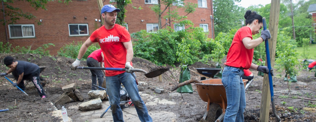 A man and a woman hold shovels as they dig in a garden