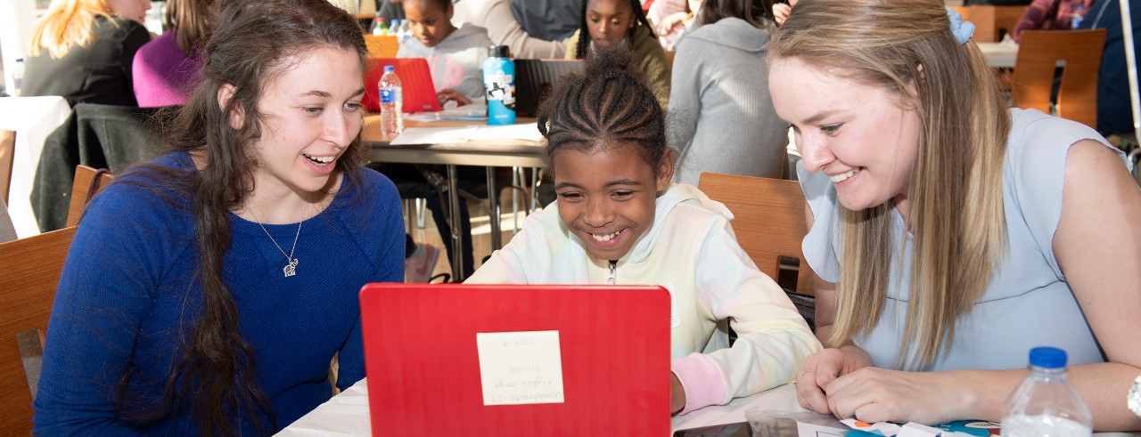 Two medical students shown with their mentee using a laptop.