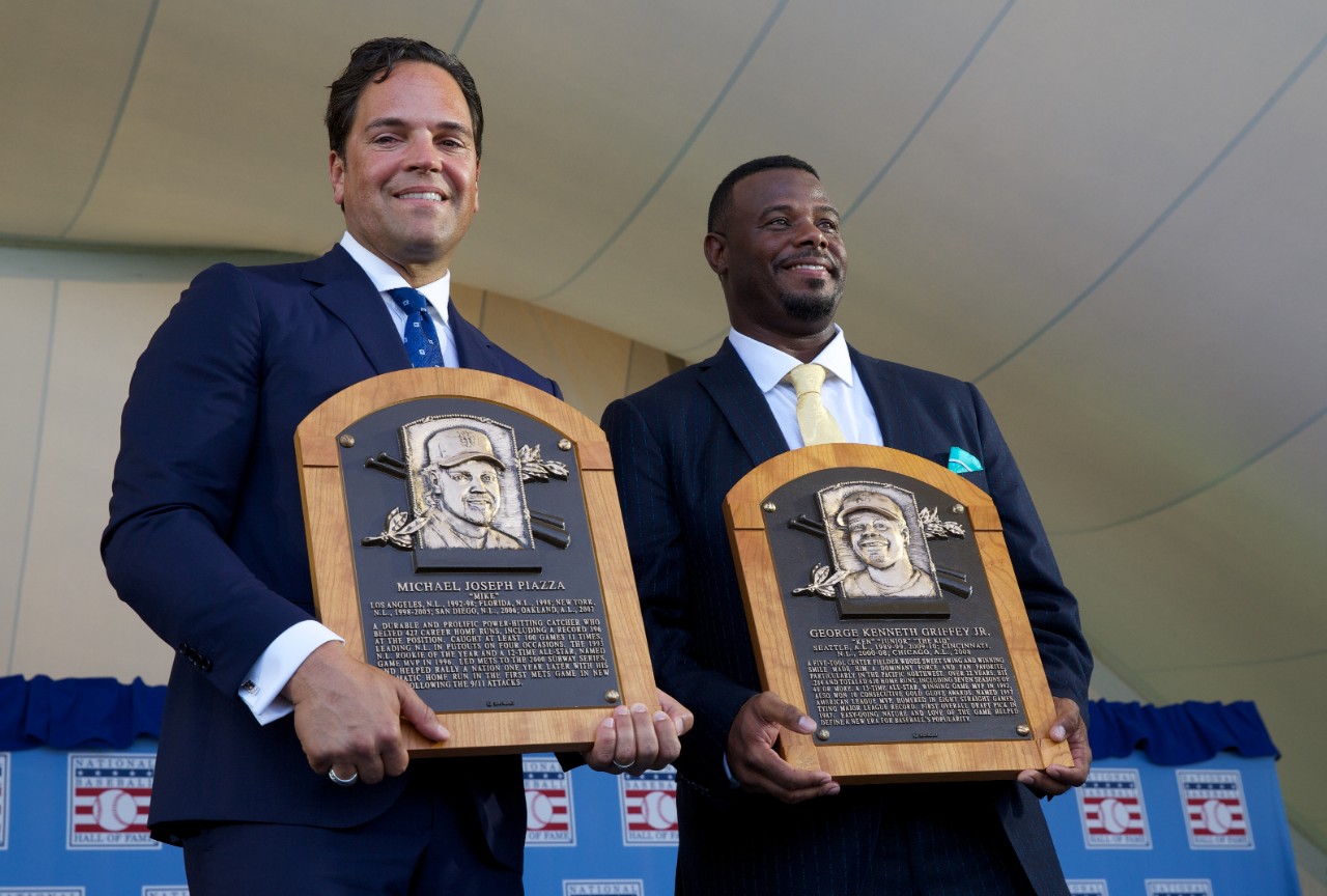 Two men in suits hold up plaques with their images on them.