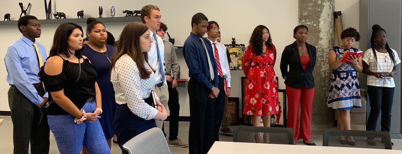 About a dozen students standing and listening attentively