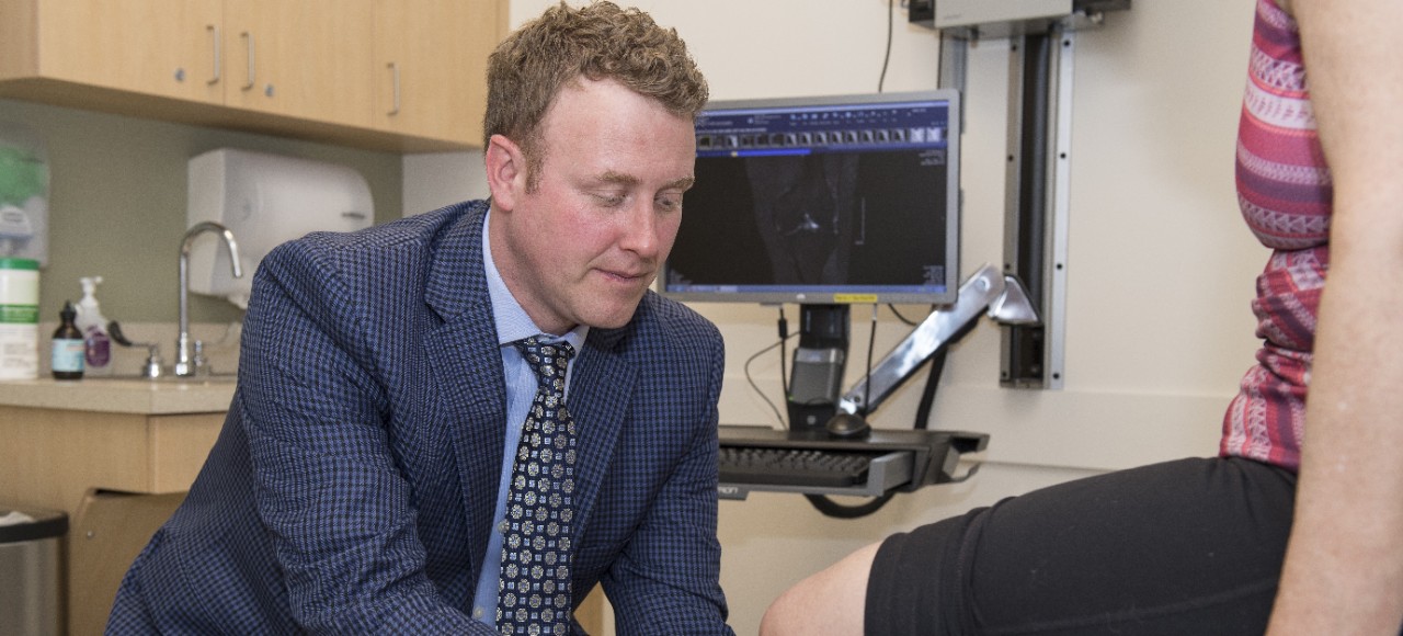Dr. Grawe, MD, examining a patient knee while the patient is lying down on an exam table    