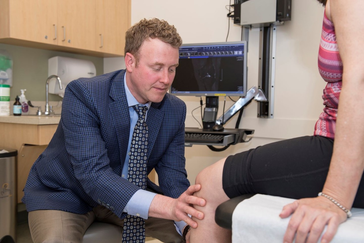 Brian Grawe, MD, examining a female patient's knee in the clinic  