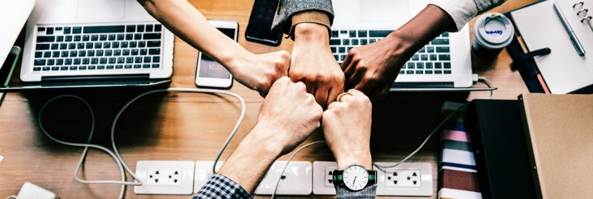 five fists bumping over a table full of computers