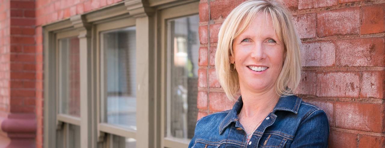 Jeanne Bruce smiling with brick wall and windows in background