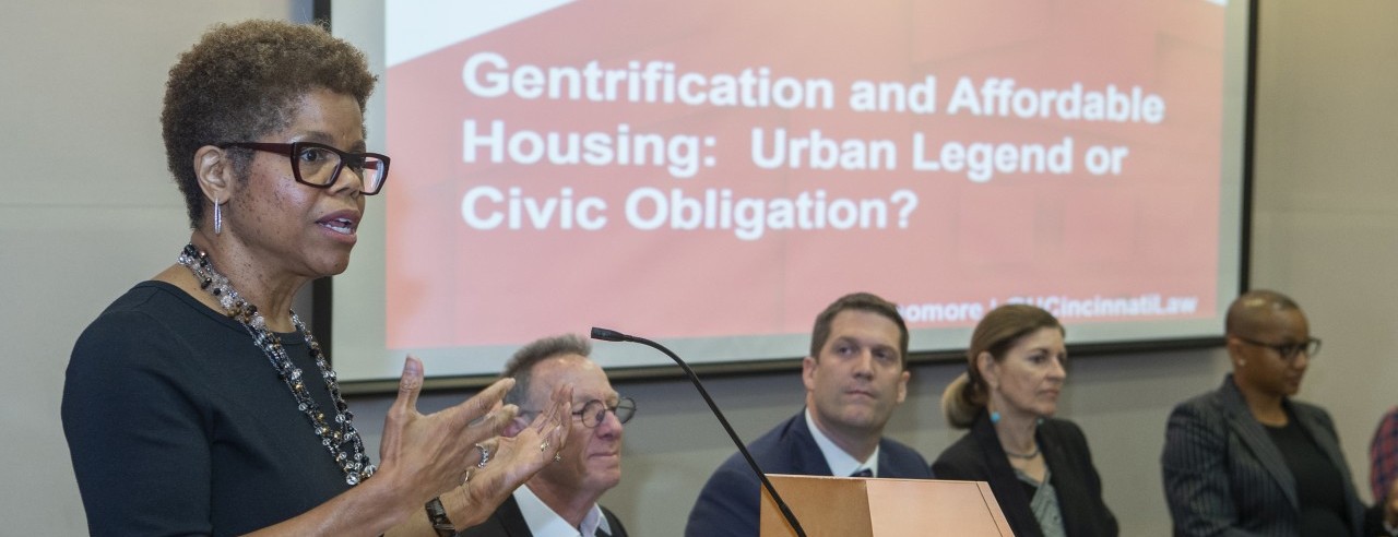 a woman stands at a podium with four people sitting behind her