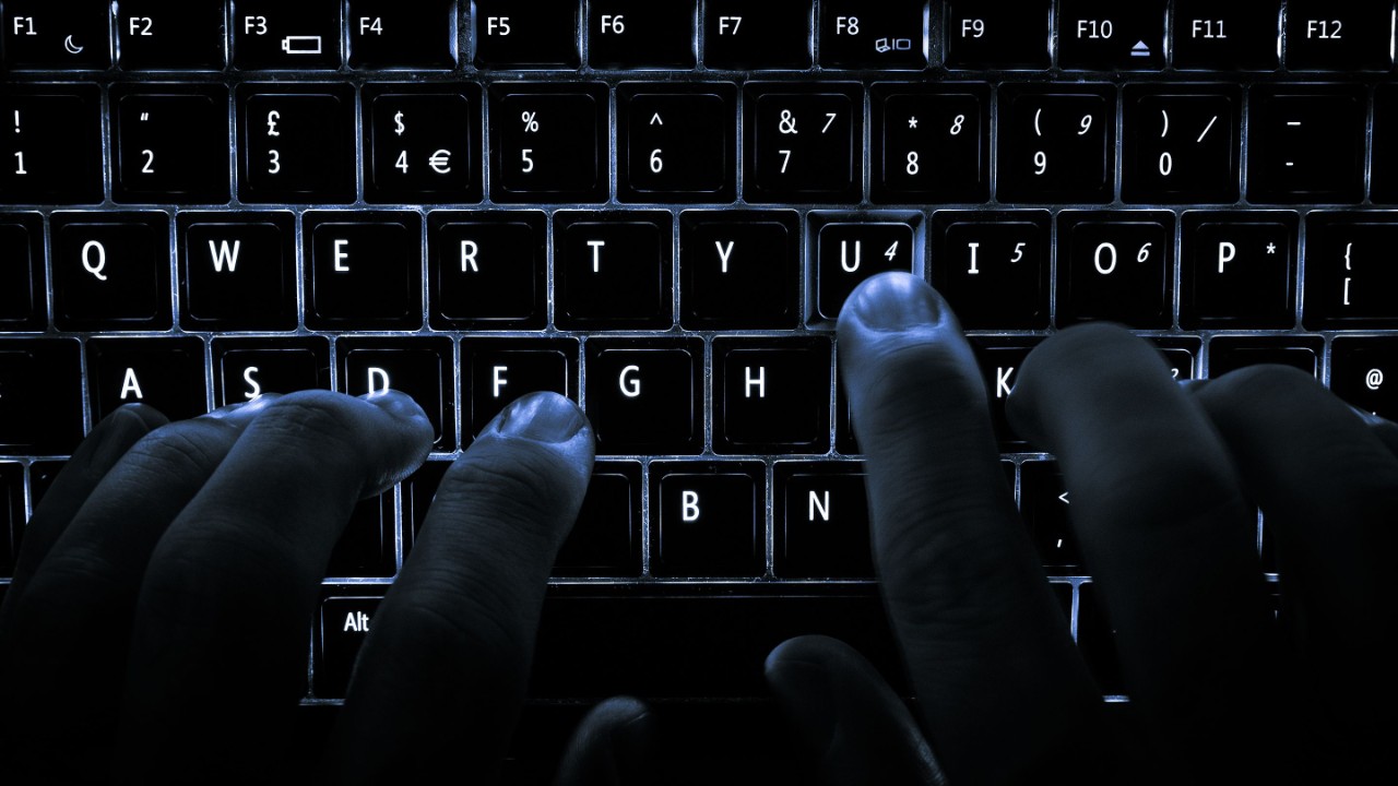 Hands type on a backlit keyboard.