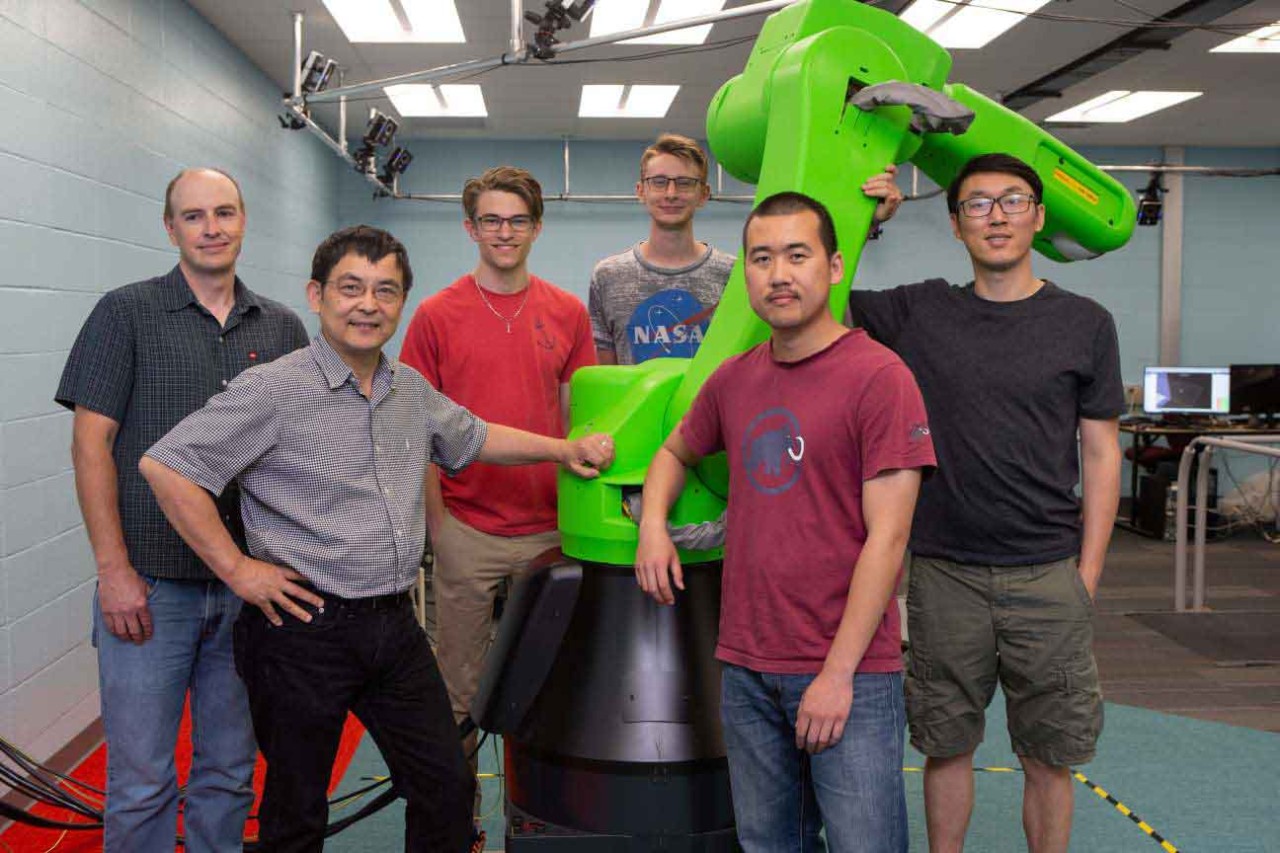 Ou Ma and his students pose in front of a large robotic arm in Ma's lab.