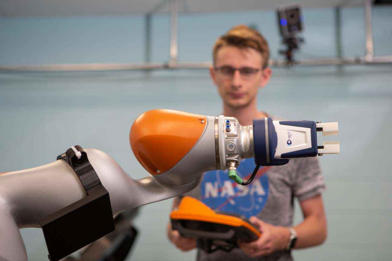 A student holds a controller in front of a robotic arm.