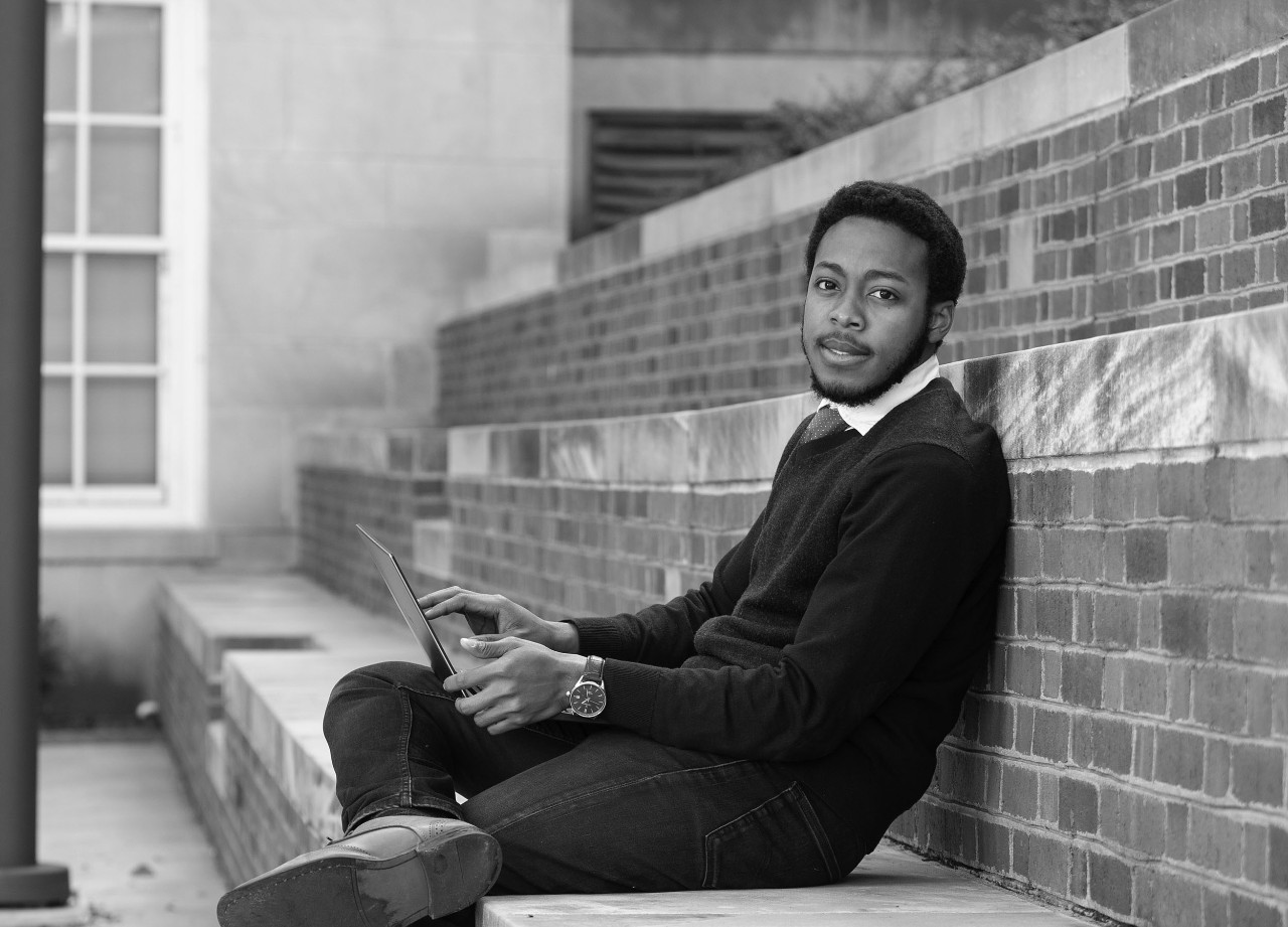 Student poses outside a campus building with laptop