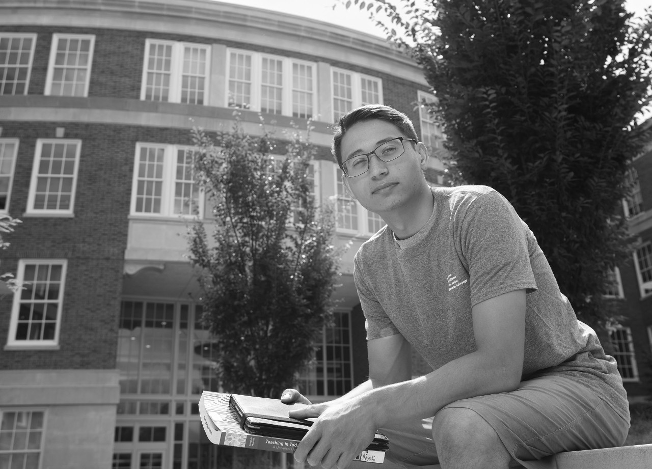 Student poses outside a campus building with books