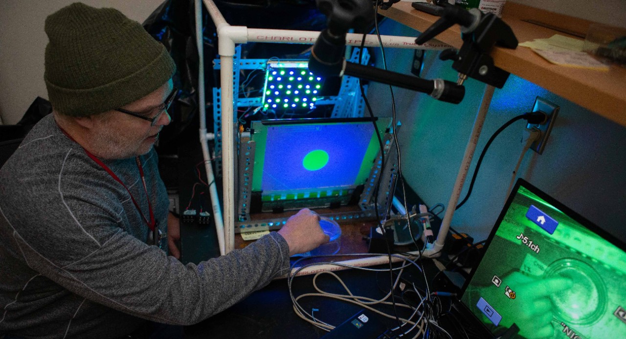 John Layne points to an LCD screen featuring a looming ball that is lighted with a panel of green and blue LED lights behind it.